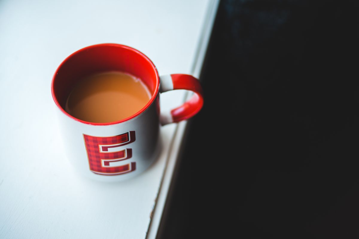 From above of white and red ceramic mug with fresh coffee and milk placed on white table