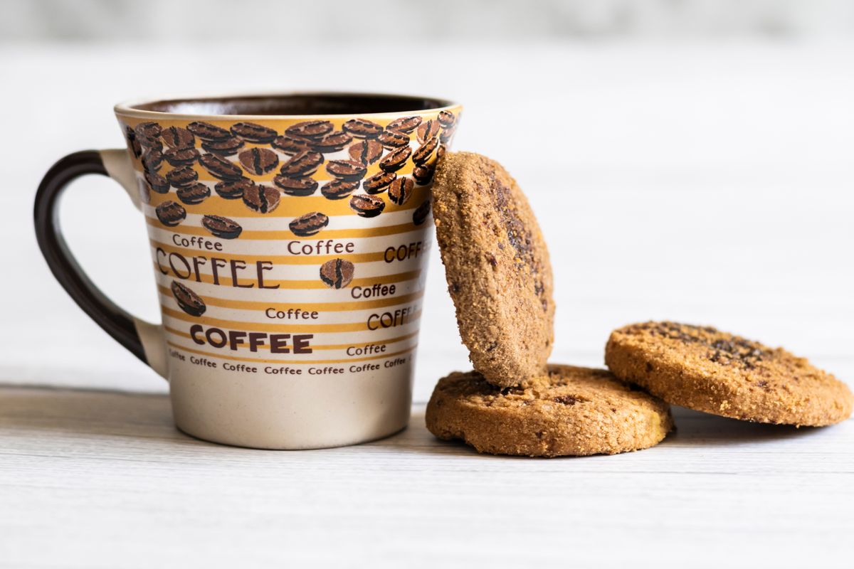 Close-up of a coffee mug and three chocolate chip cookies on a rustic wooden table.