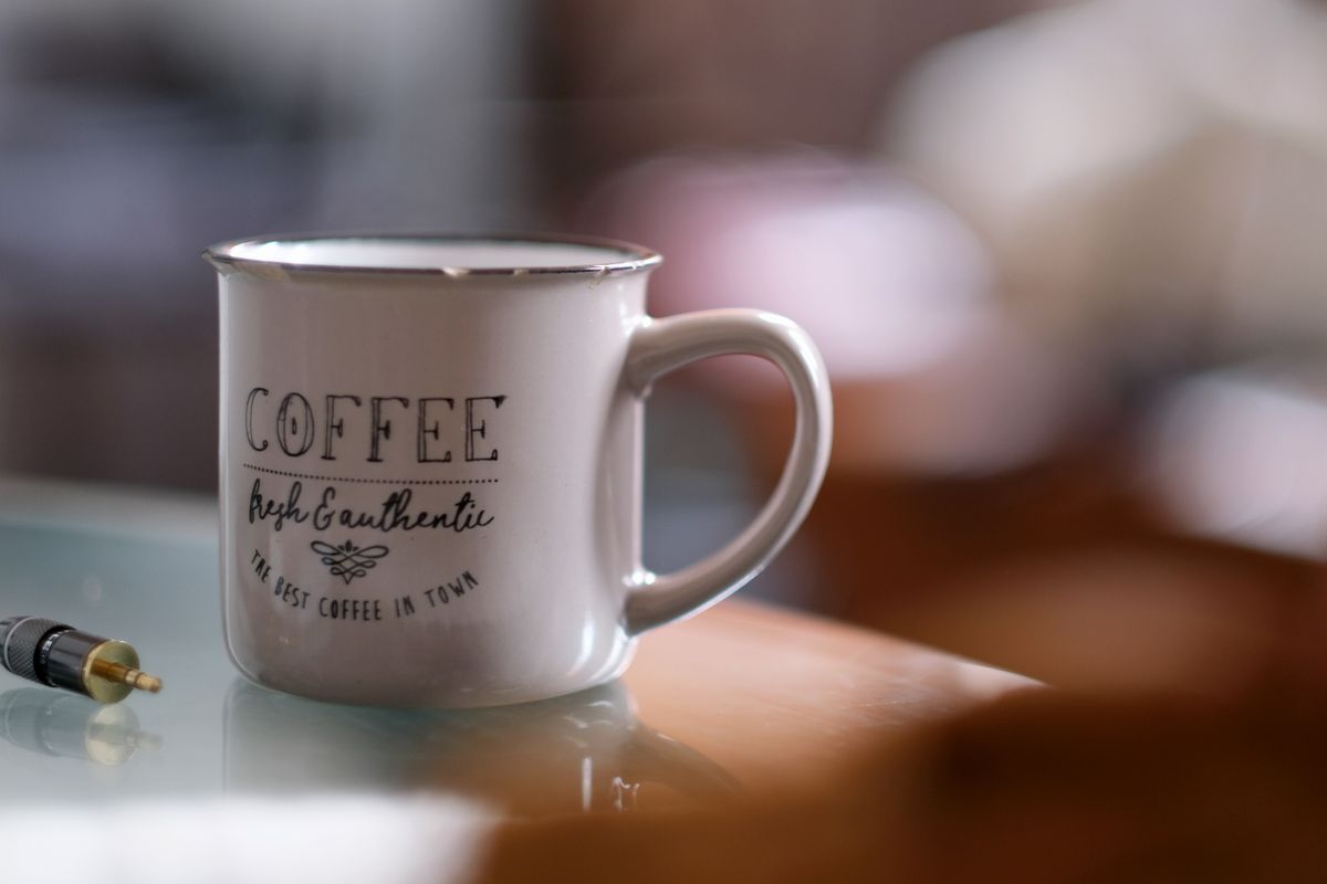 A stylish ceramic mug with coffee text on a reflective glass table in soft focus.