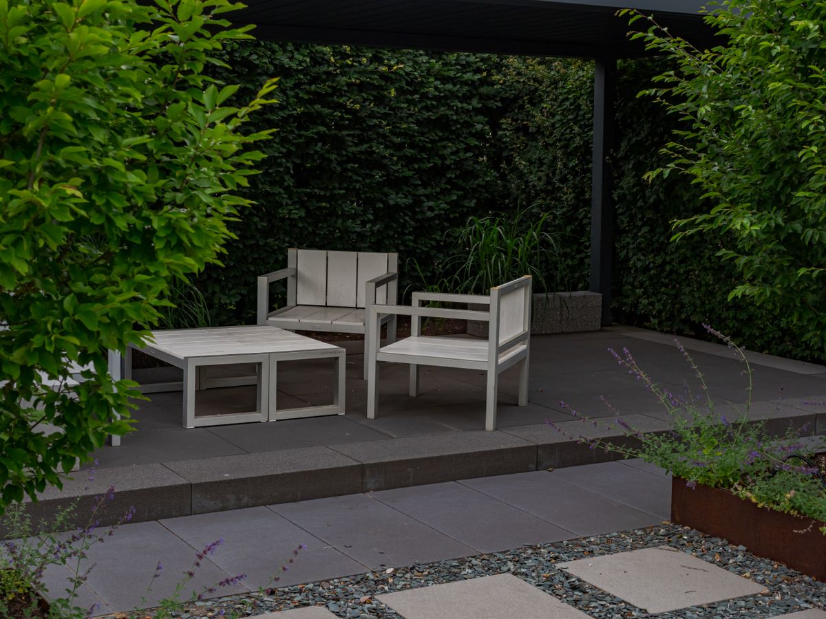 A serene outdoor patio featuring minimalist wooden furniture in a lush garden setting.