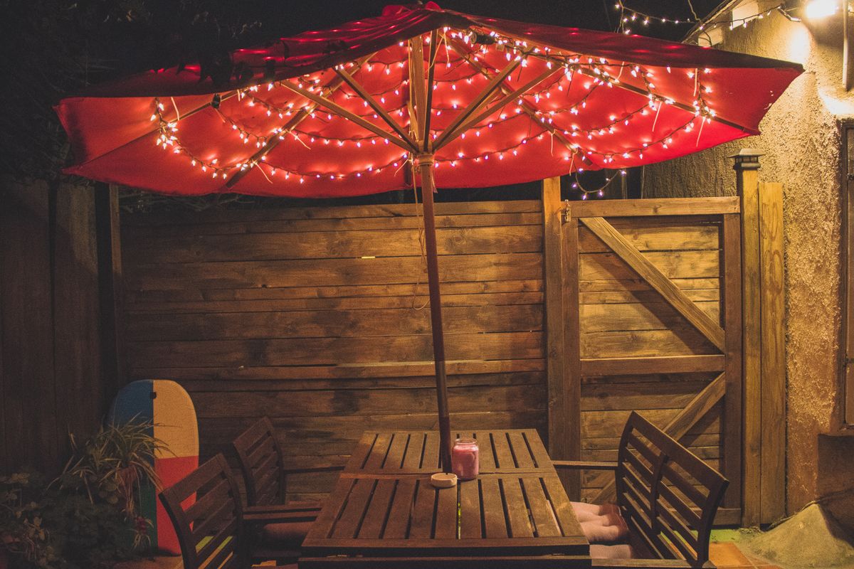 Charming outdoor dining setup with red parasol and string lights, perfect for evening gatherings.
