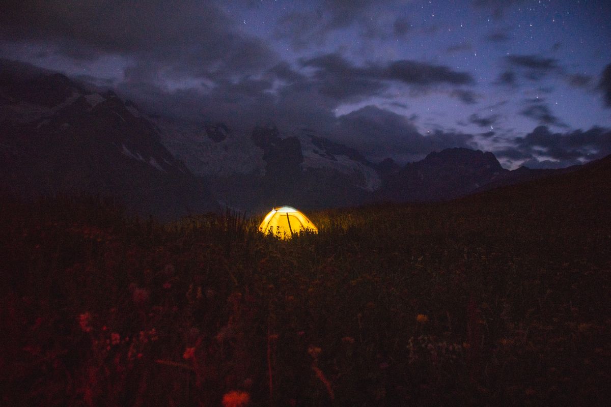 A glowing tent under a starry night sky in the scenic Caucasus Mountains, creating a serene outdoor camping experience.