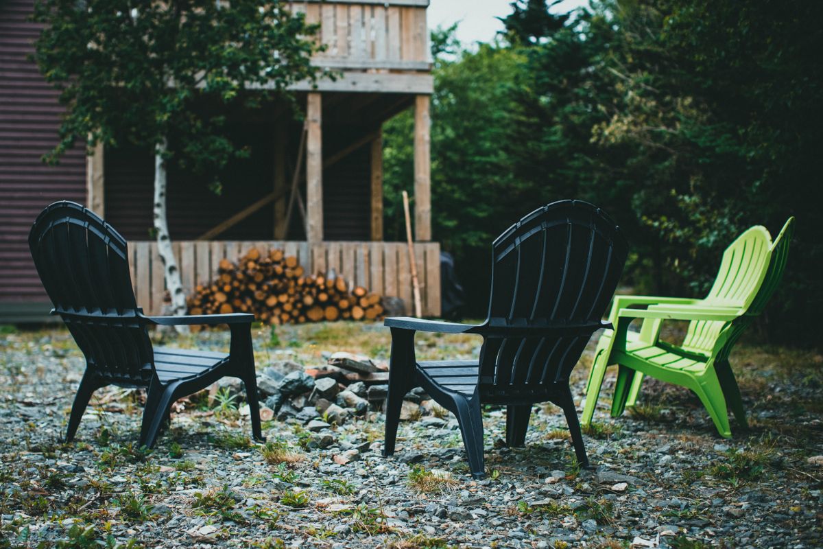 Three Adirondack chairs around a fire pit in a rustic backyard setting, perfect for outdoor relaxation.