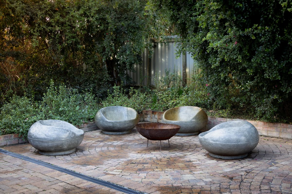 An inviting outdoor patio with stone seating and a fire pit, surrounded by lush greenery.