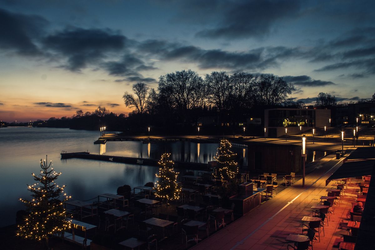 A tranquil riverside patio lit with Christmas lights during sunset, showcasing a serene evening ambiance.