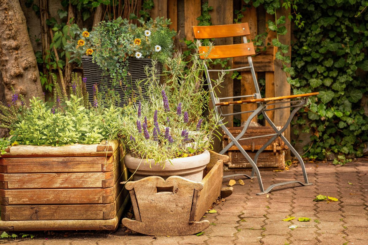 Charming rustic garden patio featuring wooden planters filled with vibrant flowers and a folding chair.
