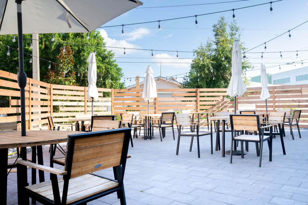 A serene outdoor cafe patio with wooden tables and chairs, shaded by umbrellas and decorated with string lights.