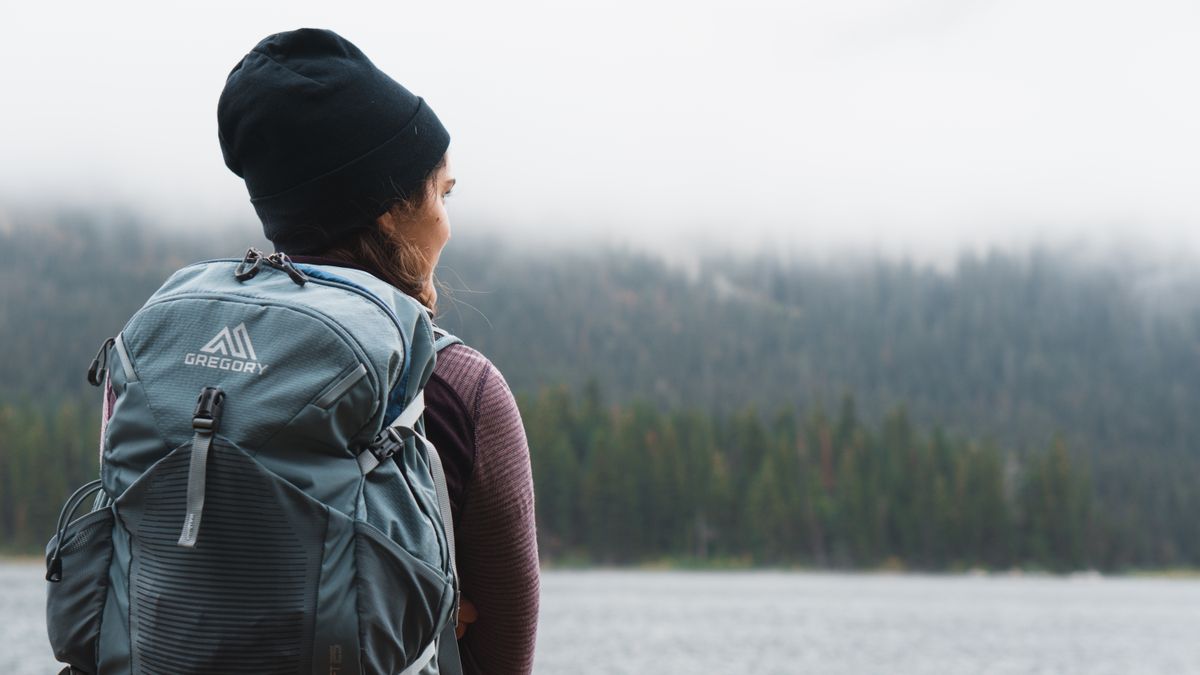 Woman with backpack overlooking a foggy forest by a lake, capturing tranquility and exploration.