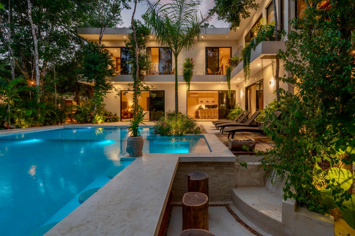 Modern luxury villa with a lit pool and tropical garden. Evening view.