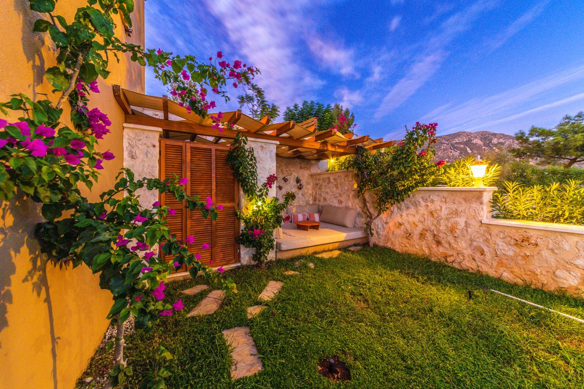 A cozy garden patio with vibrant flowers under a wooden pergola at twilight.