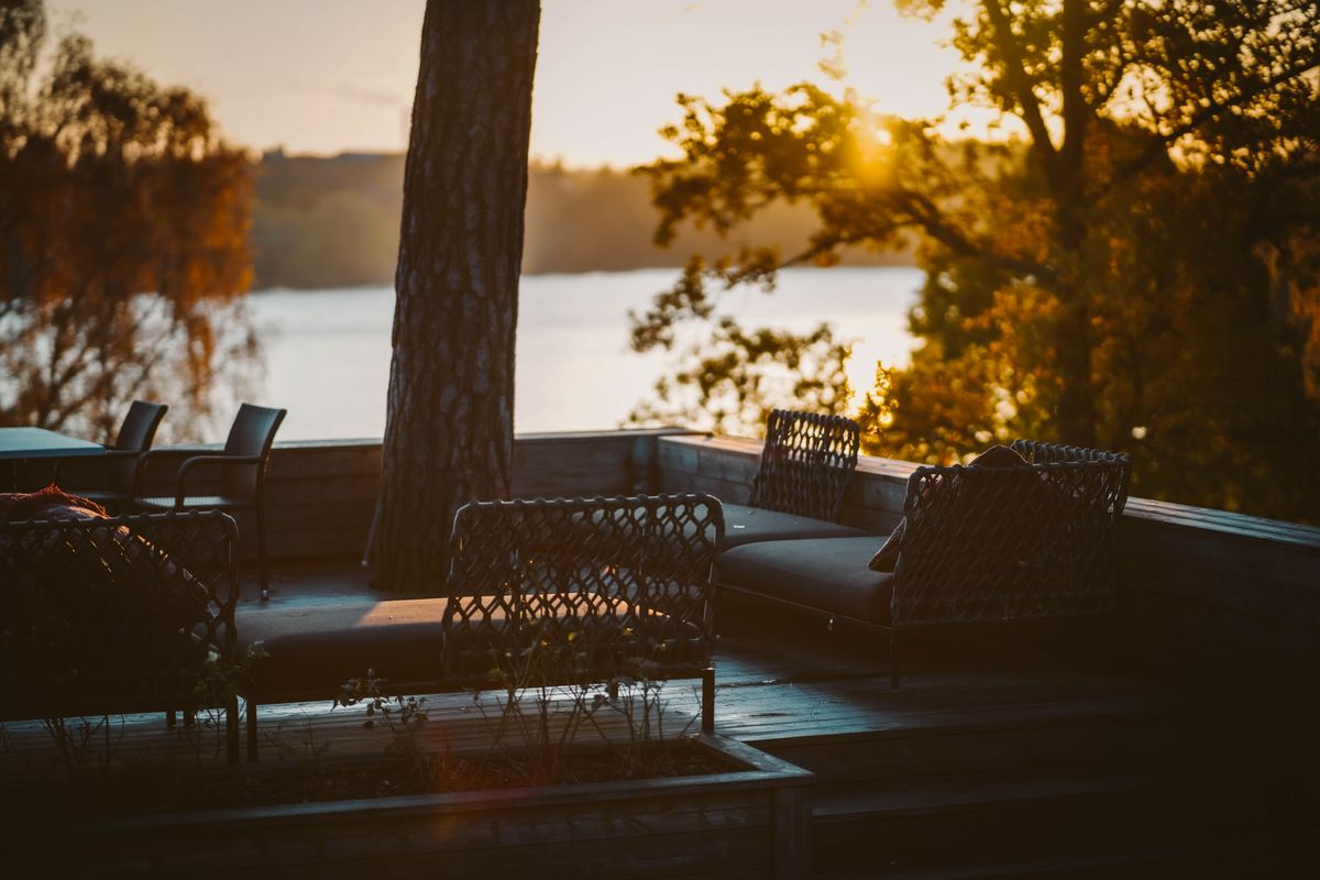 A serene patio setting with woven furniture overlooks a calm lake in Solna, Sweden during summer sunset.