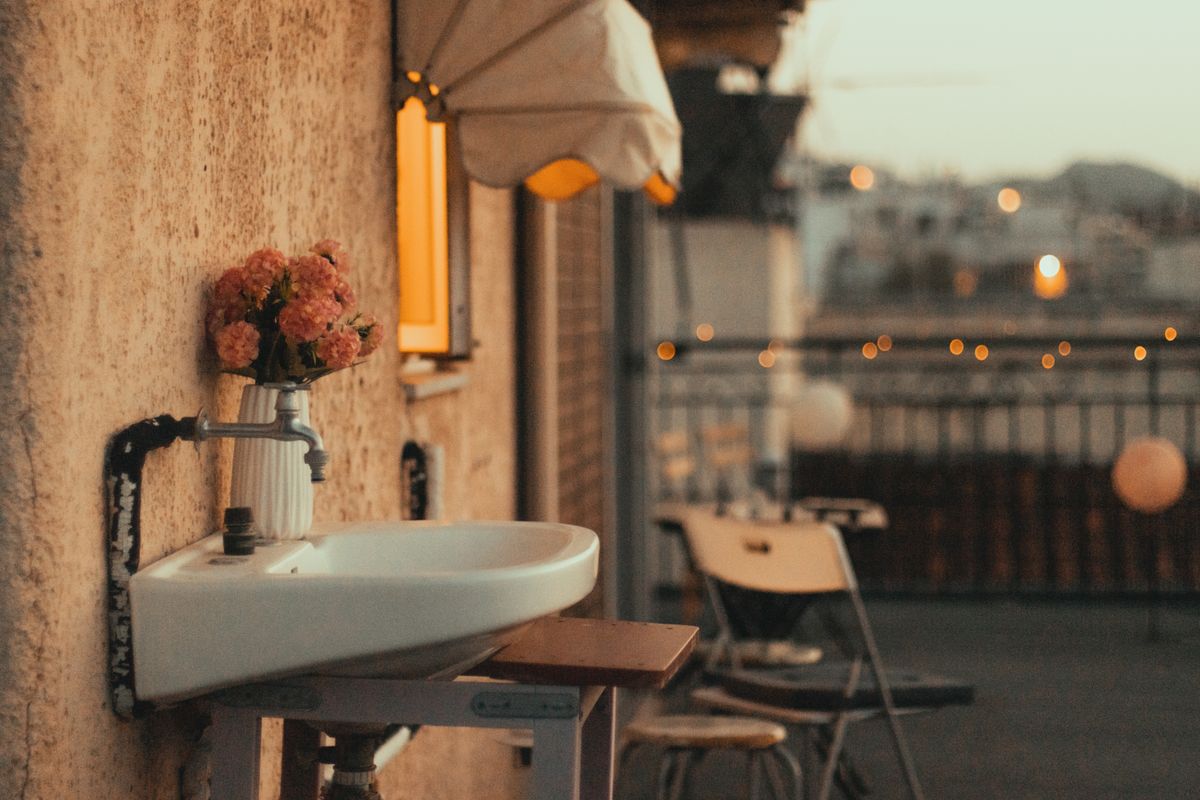 Cozy outdoor setting with sink, flowers, chairs, and evening city lights.