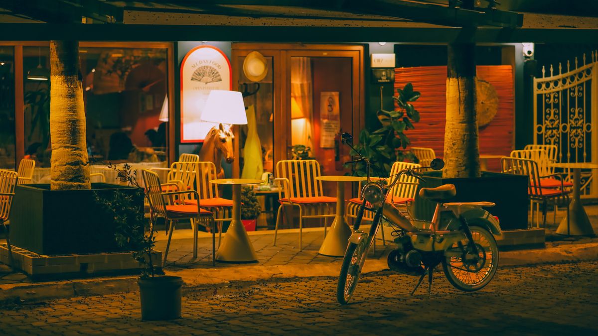 Charming evening shot of a cozy outdoor restaurant with a retro scooter parked nearby and ambient lighting.