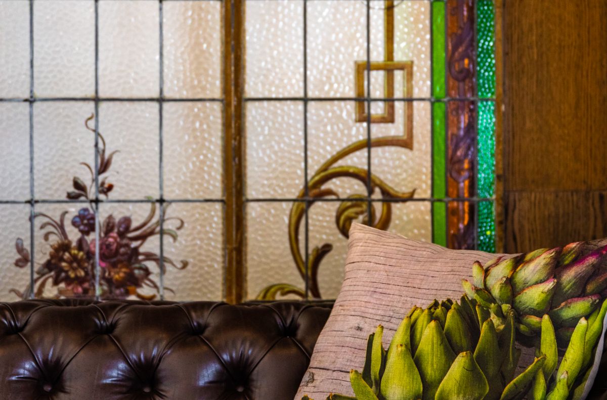 A sophisticated leather sofa with a decorative artichoke pillow, set against a stained glass backdrop.