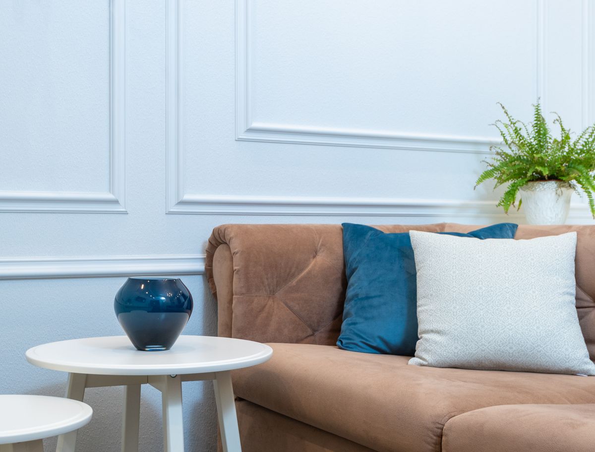 Brown sofa with cushions beside a table with a vase in a cozy living room.