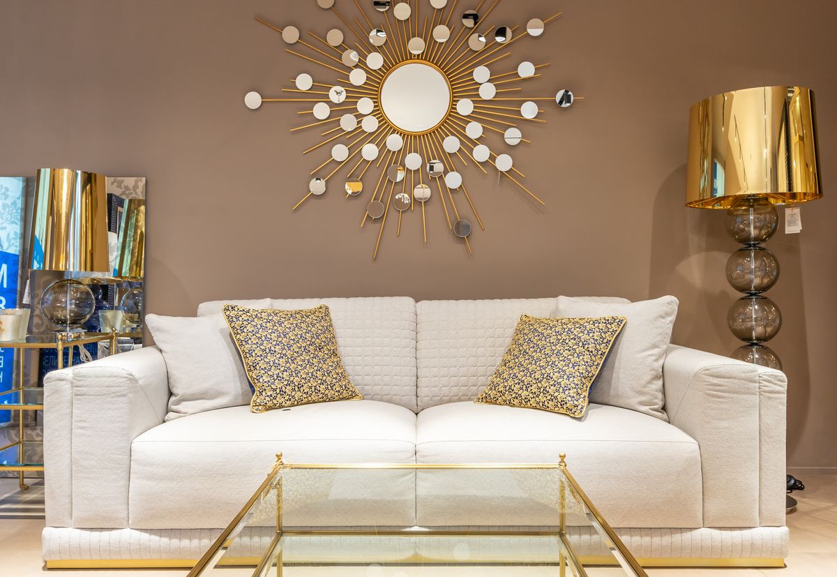 Comfortable white sofa with pillows placed near with floor lamp at wall with decorative elements in stylish living room of apartment