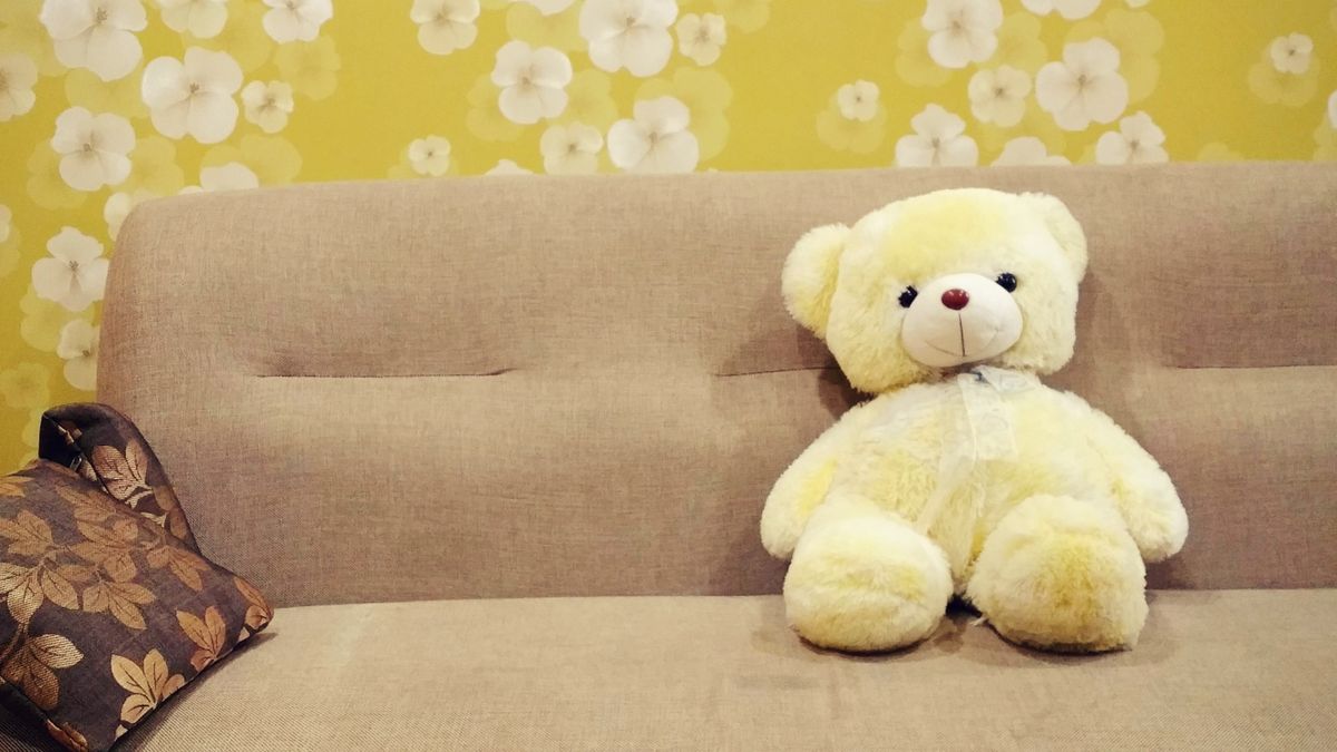 A cozy yellow teddy bear on a sofa with floral wallpaper, ideal for kids' room decor.