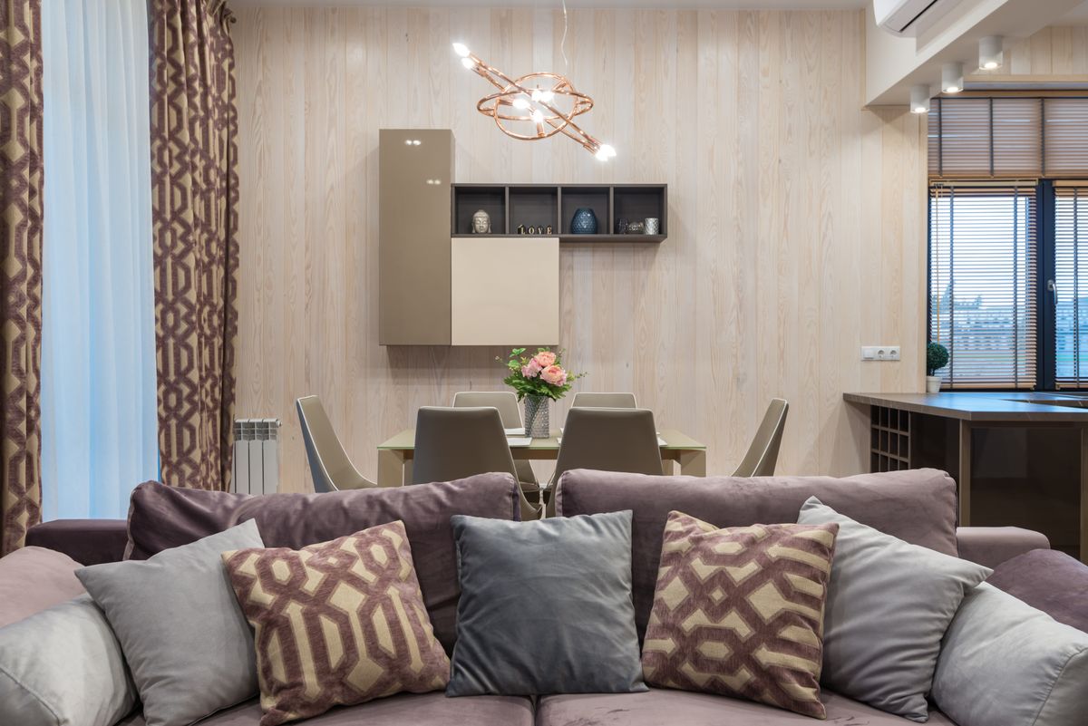 Comfortable couch with cushions placed in living room near dining zone in modern apartment