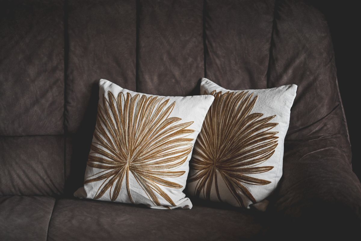 Pair of decorative pillows with leaf patterns on a brown sofa, creating a stylish home interior look.