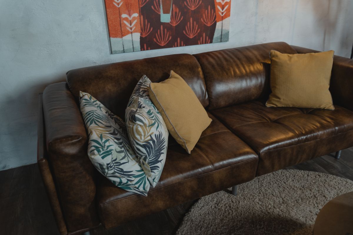 Warm brown leather sofa with patterned and plain pillows in a cozy living room setting.