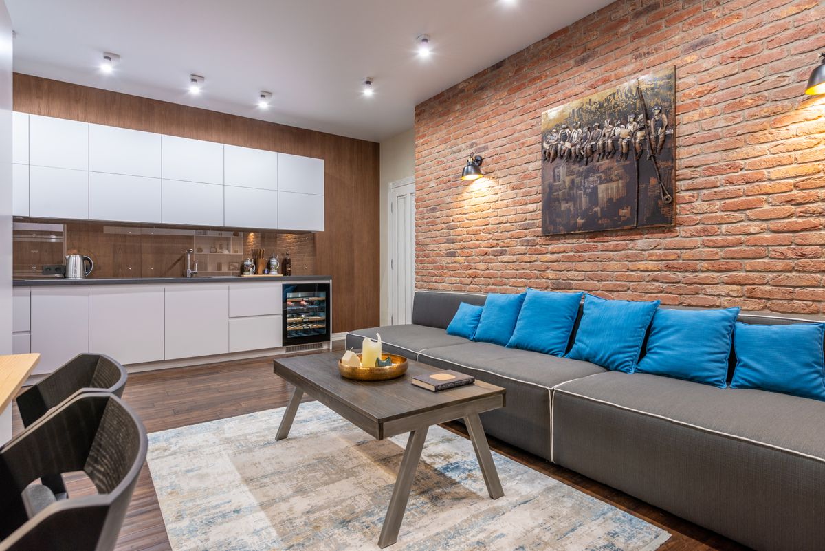 Contemporary living room and kitchen interior with table and sofa under painting with engraving in house with shiny lamps