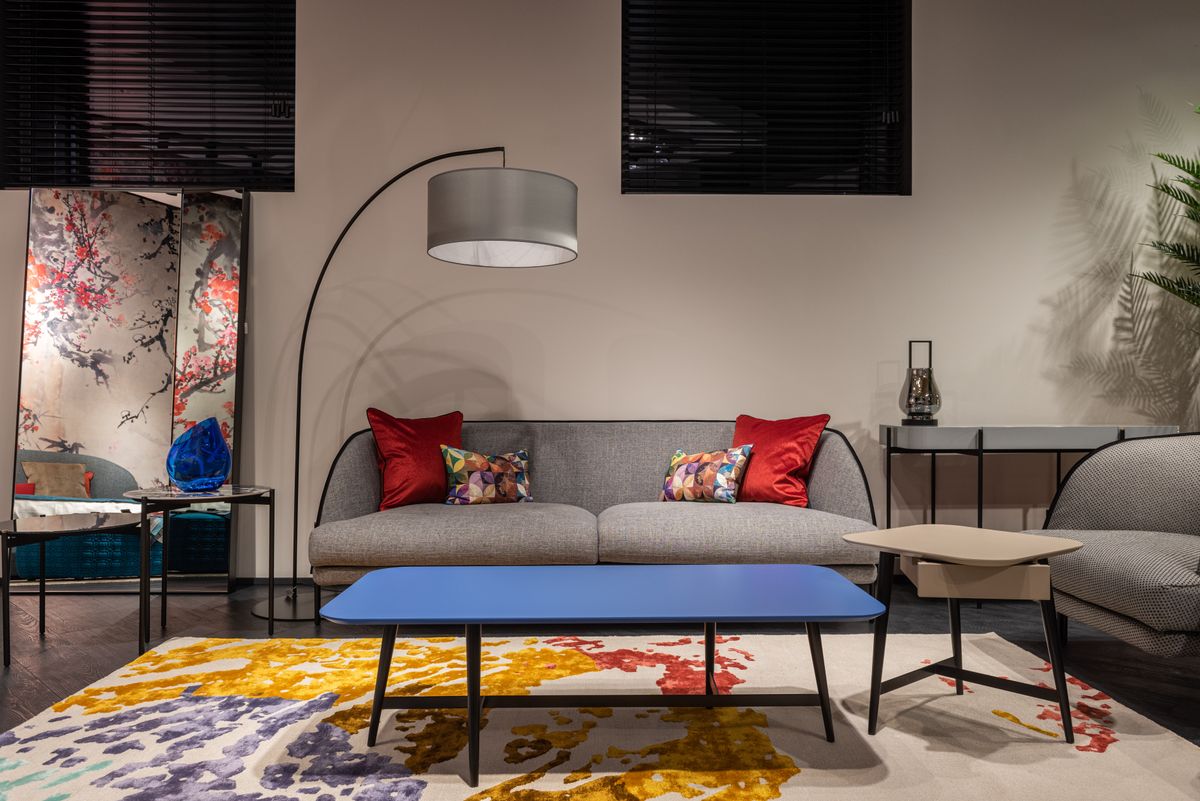 Comfortable sofa with colorful cushions placed at wall near armchair and table on carpet in spacious living room with lamp