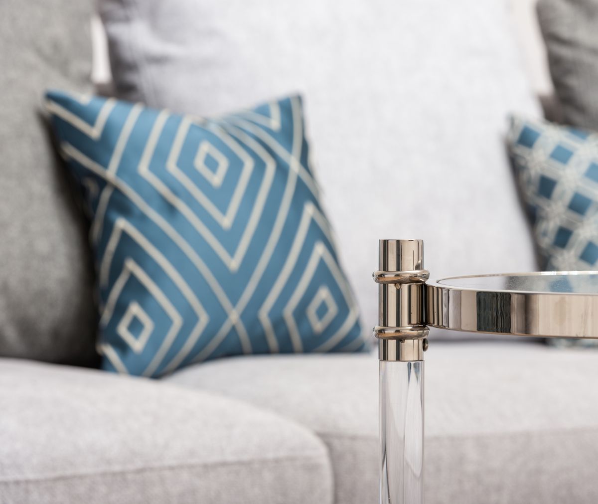 Metal and glass table against soft sofa with ornamental square shaped cushions in room at home