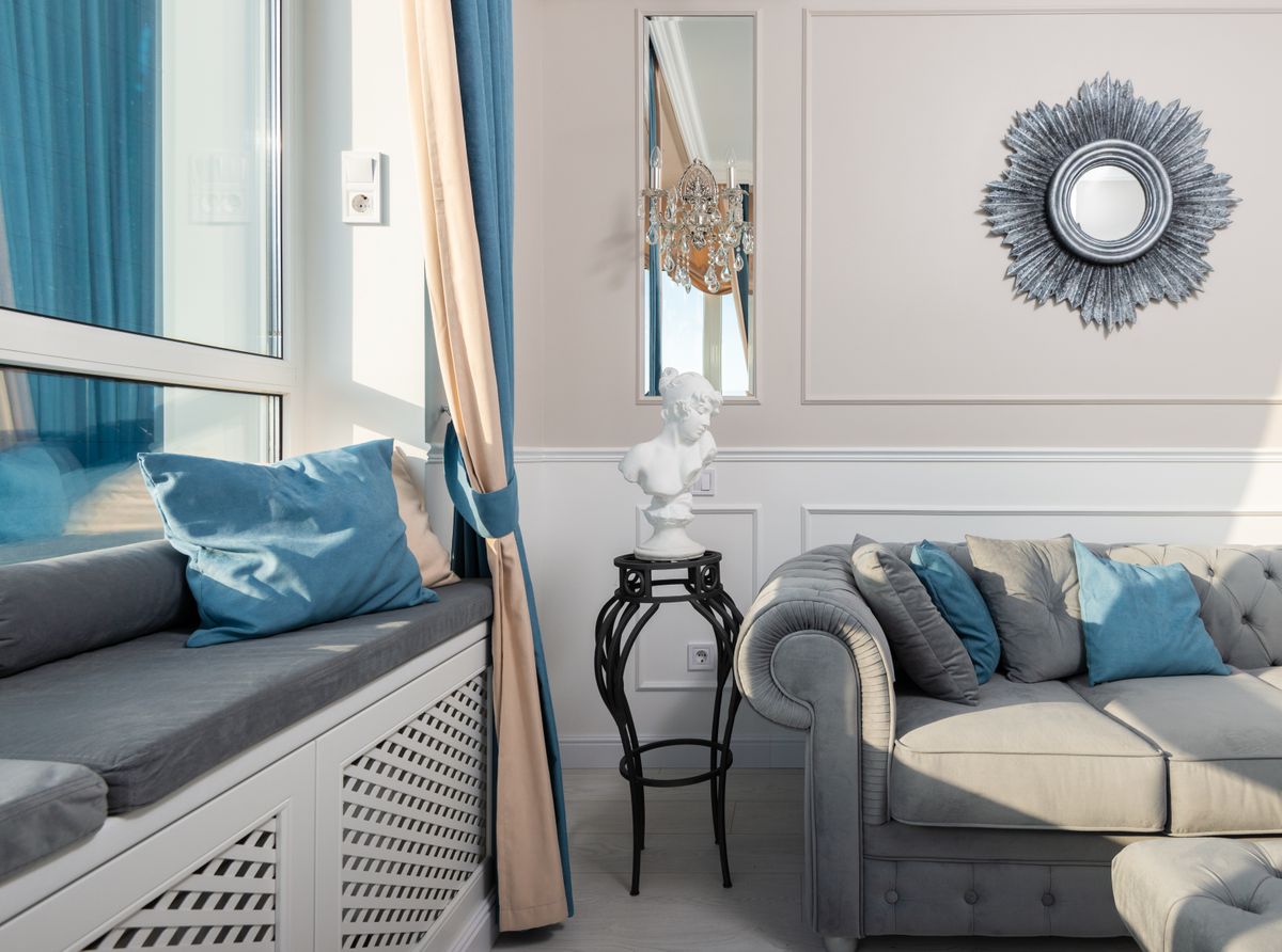 Contemporary room interior with decorative cushions on sofa under mirror on sunny day at home