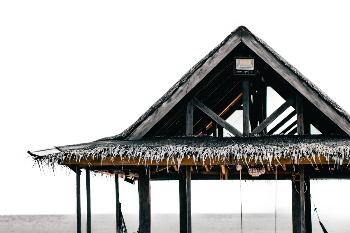 A rustic wooden gazebo by the coast, featuring solar lighting and a straw roof.