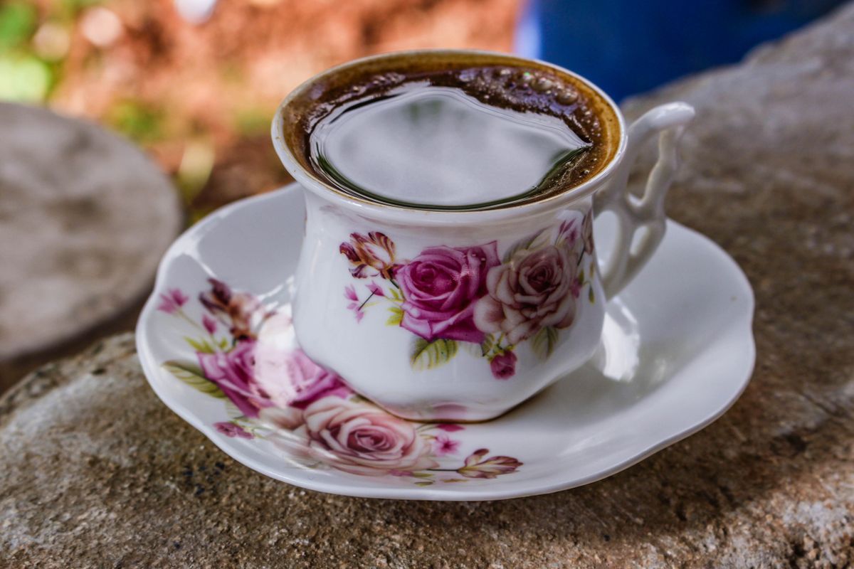 Porcelain cup of coffee with floral design on a weathered stone surface.