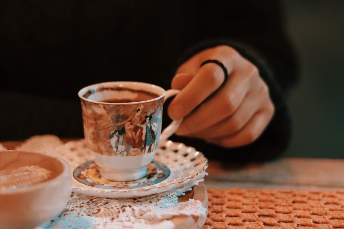 A close-up of a hand holding a vintage cup with artistic design, set on a table.