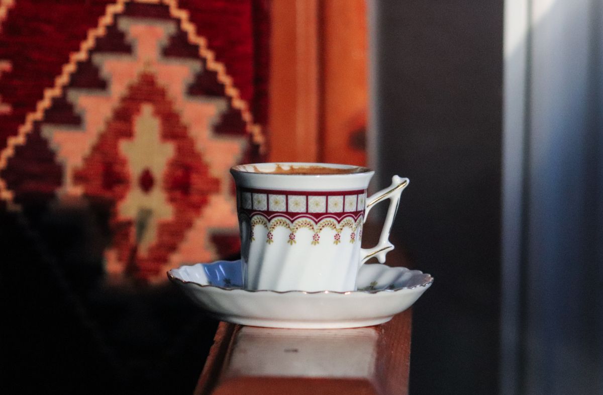 Ornate coffee cup with saucer on a wooden railing, set against a patterned background.