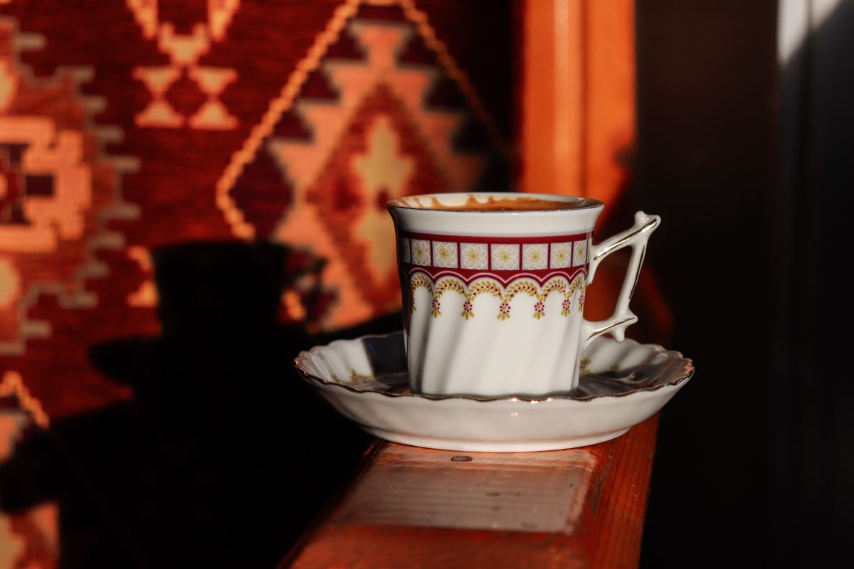 A decorative coffee cup on a wooden surface with a warm, patterned background.