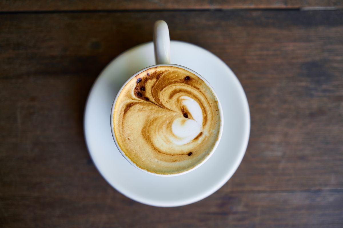 Top view of a coffee cup with intricate latte art on a white saucer.