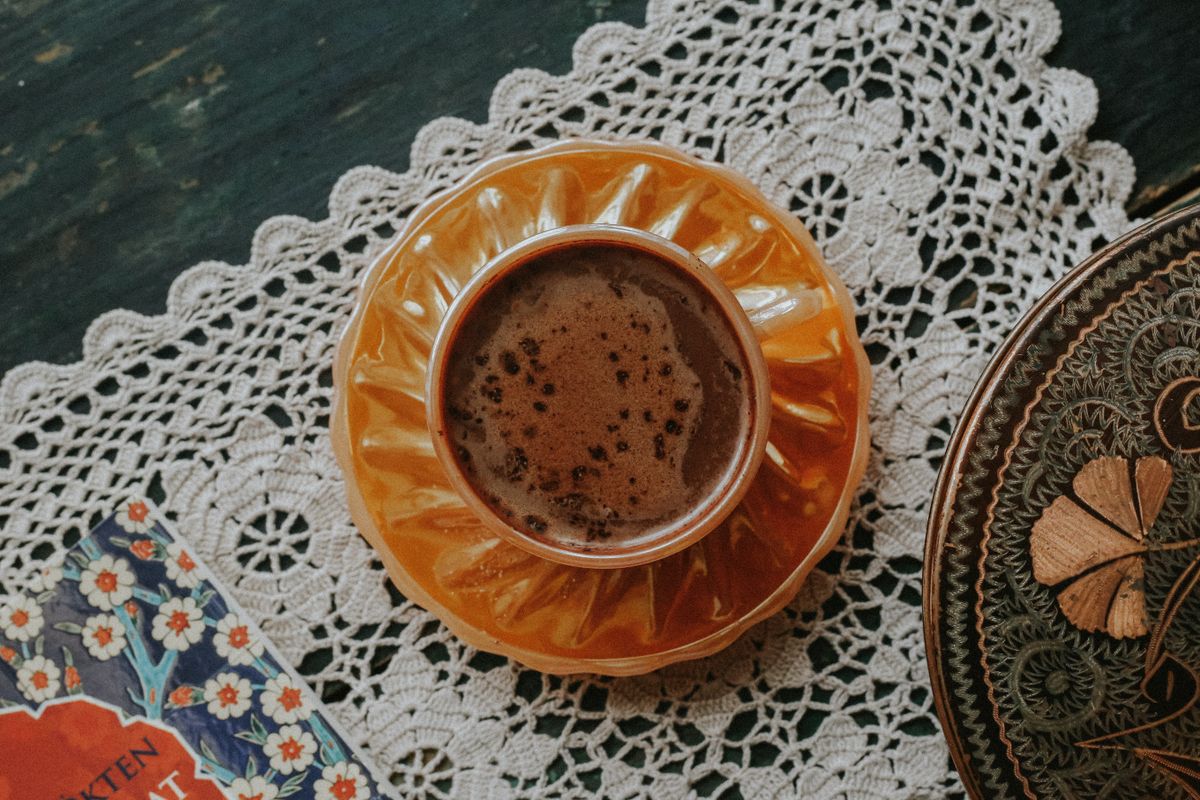 Top view of a vintage coffee cup on a lace tablecloth, beside a decorative plate.
