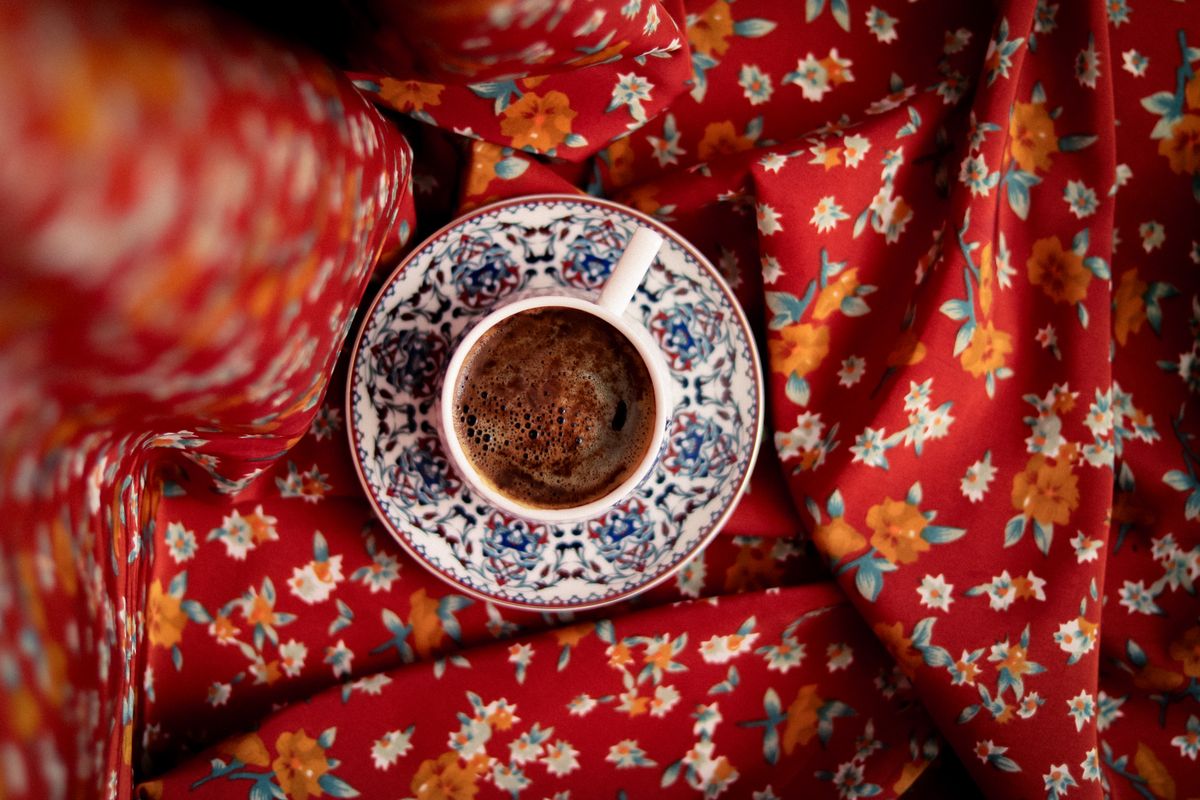Top view of a coffee cup on ornate porcelain over red floral fabric, vibrant and inviting.