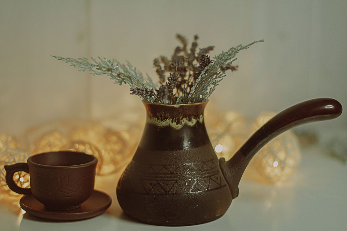 Cozy indoor setup of a brown ceramic coffee pot and cup with decorative twigs in a warm ambient lighting.