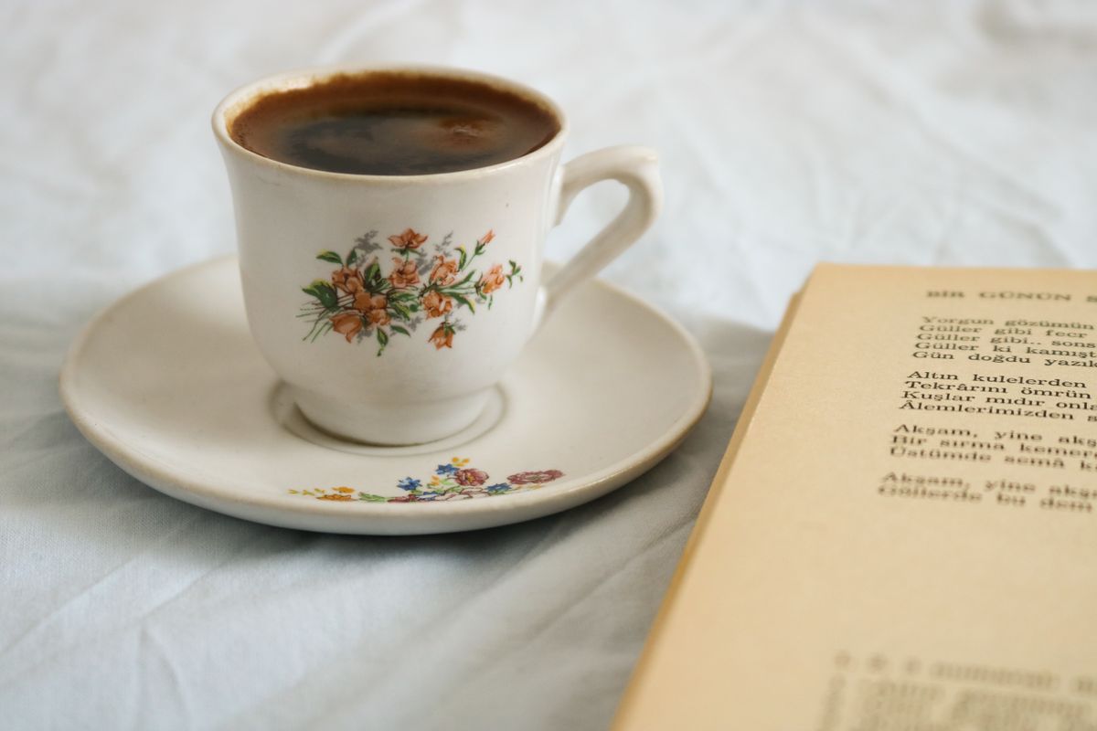 Close-up of a floral porcelain cup filled with black coffee alongside an open book, creating a serene and relaxing scene.