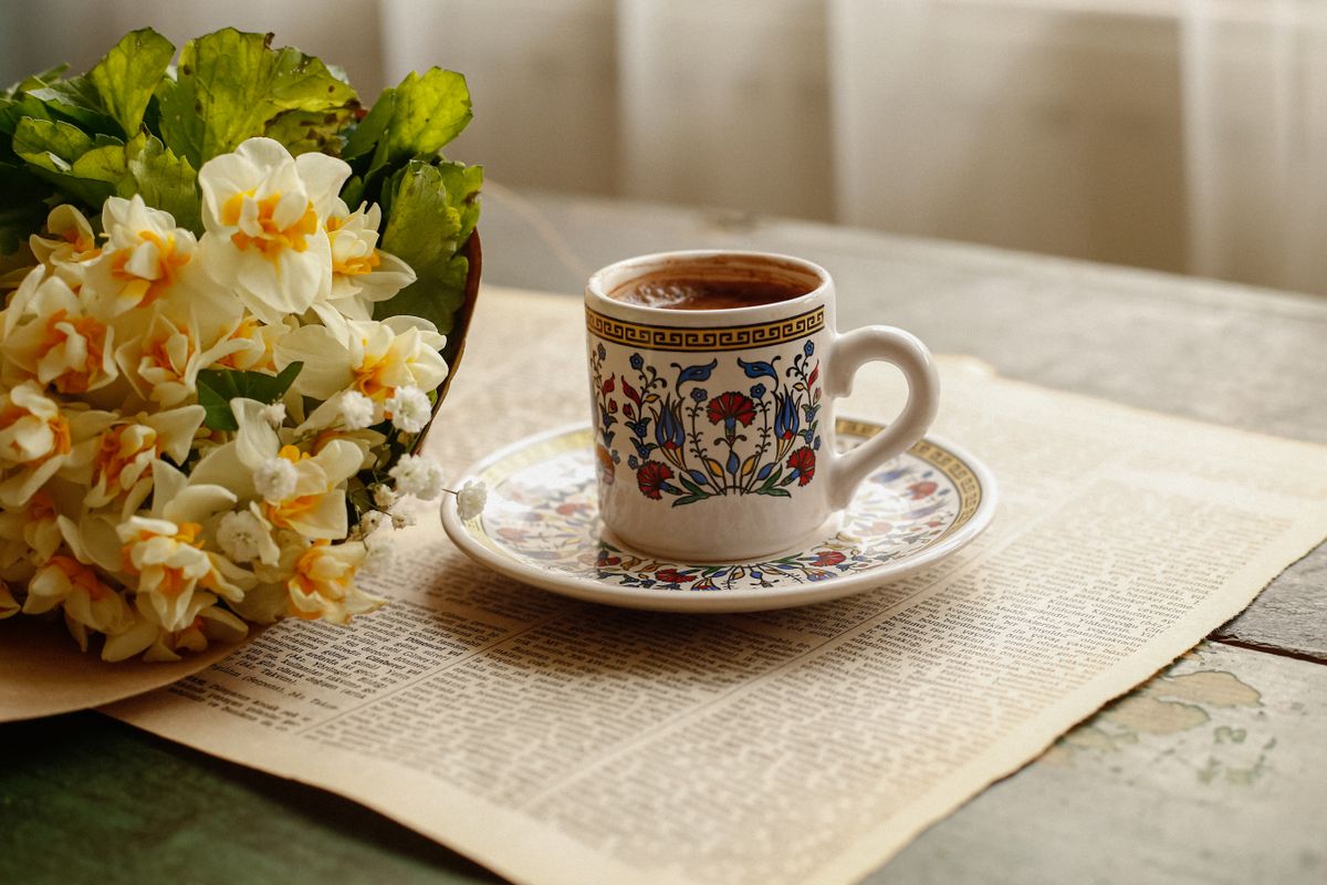 Artistic floral tea cup with coffee beside a daffodil bouquet on vintage paper.