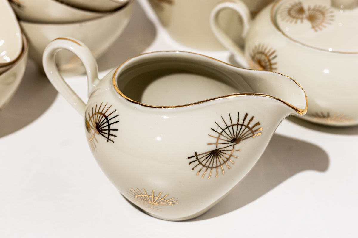 Close-up of a white ceramic creamer featuring a gold decorative pattern. Perfect for tea or coffee settings.