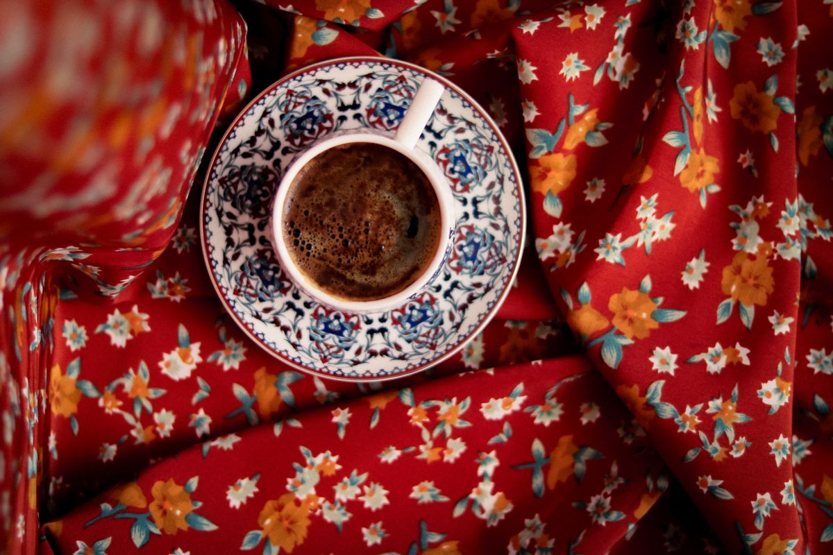 Top view of a coffee cup with intricate design on vibrant floral red fabric, creating a warm and inviting scene.