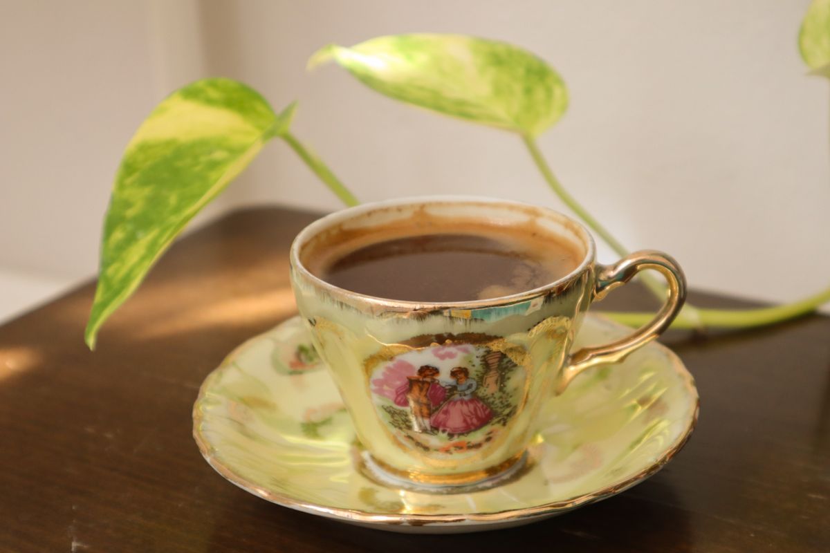 Decorative porcelain teacup with black coffee and green leaves on a wooden table.