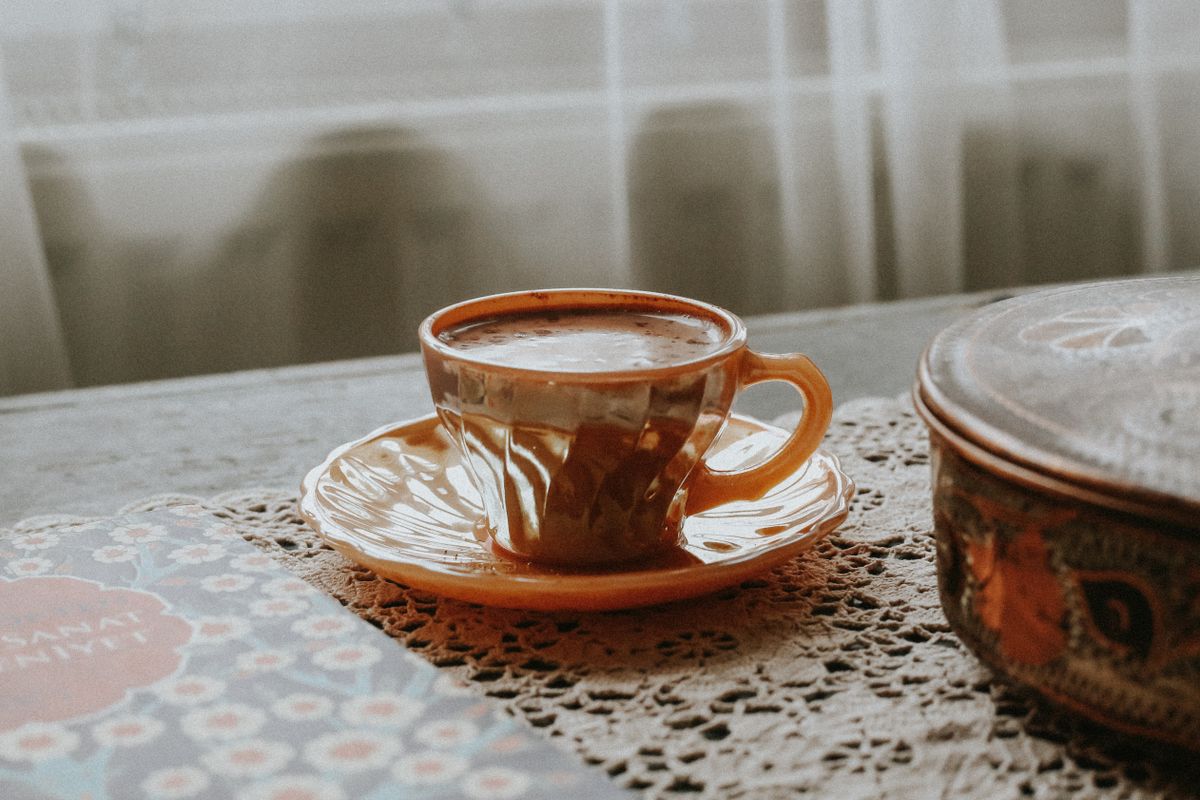 A warm, vintage-style coffee cup sits on a lace tablecloth, creating a cozy and nostalgic ambiance.