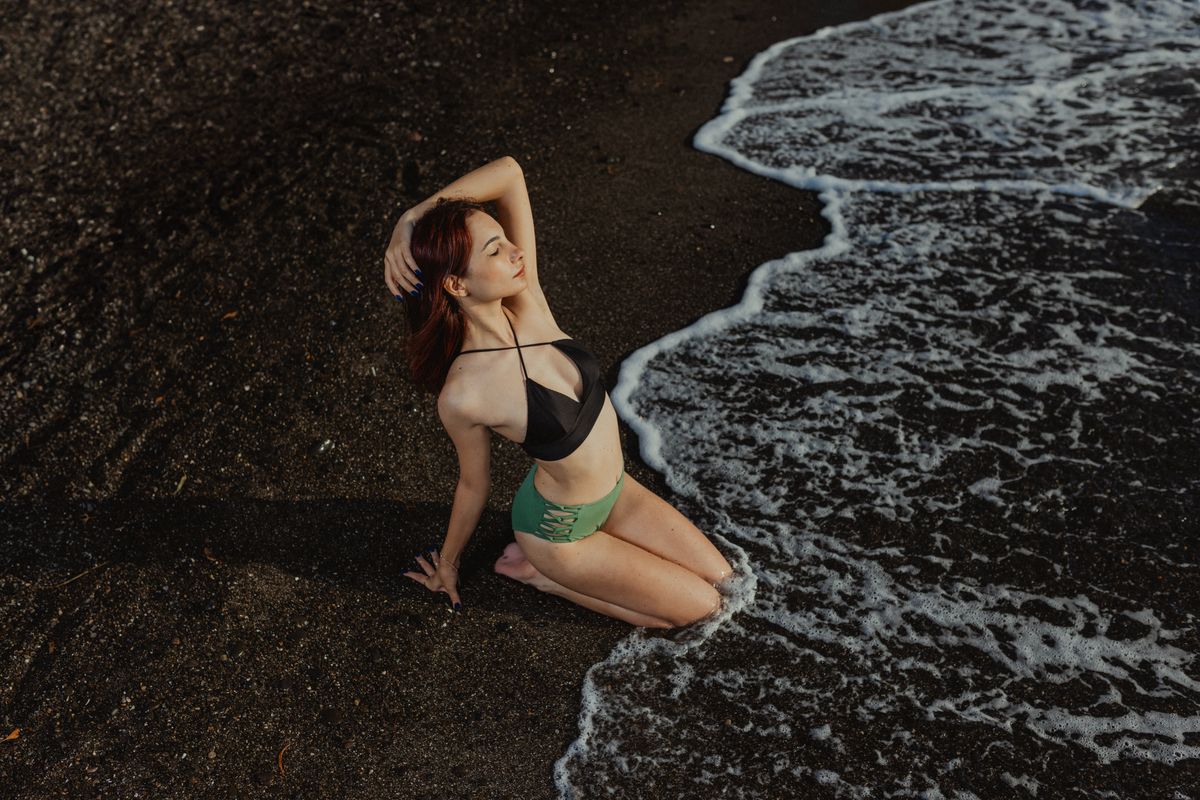 Woman in black bikini enjoying the ocean waves on a black sand beach.