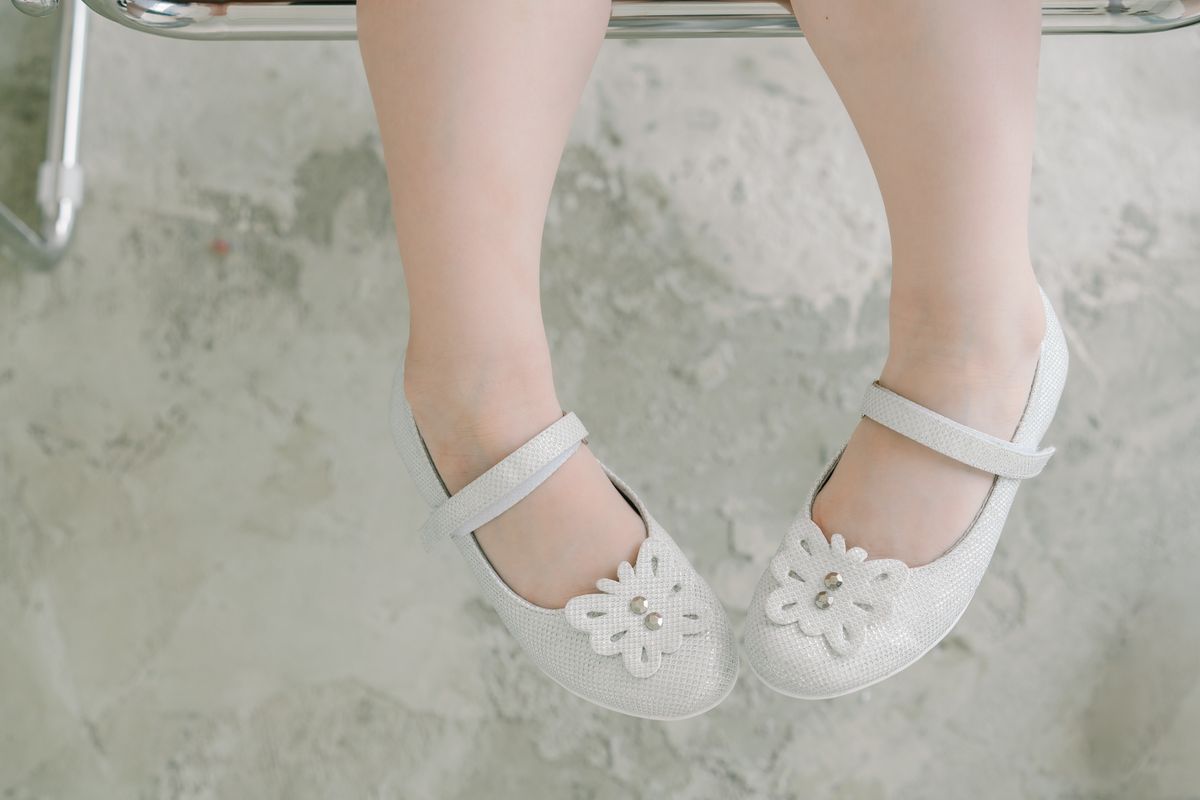 Close-up of child's feet in white doll shoes with floral designs, resting indoors.