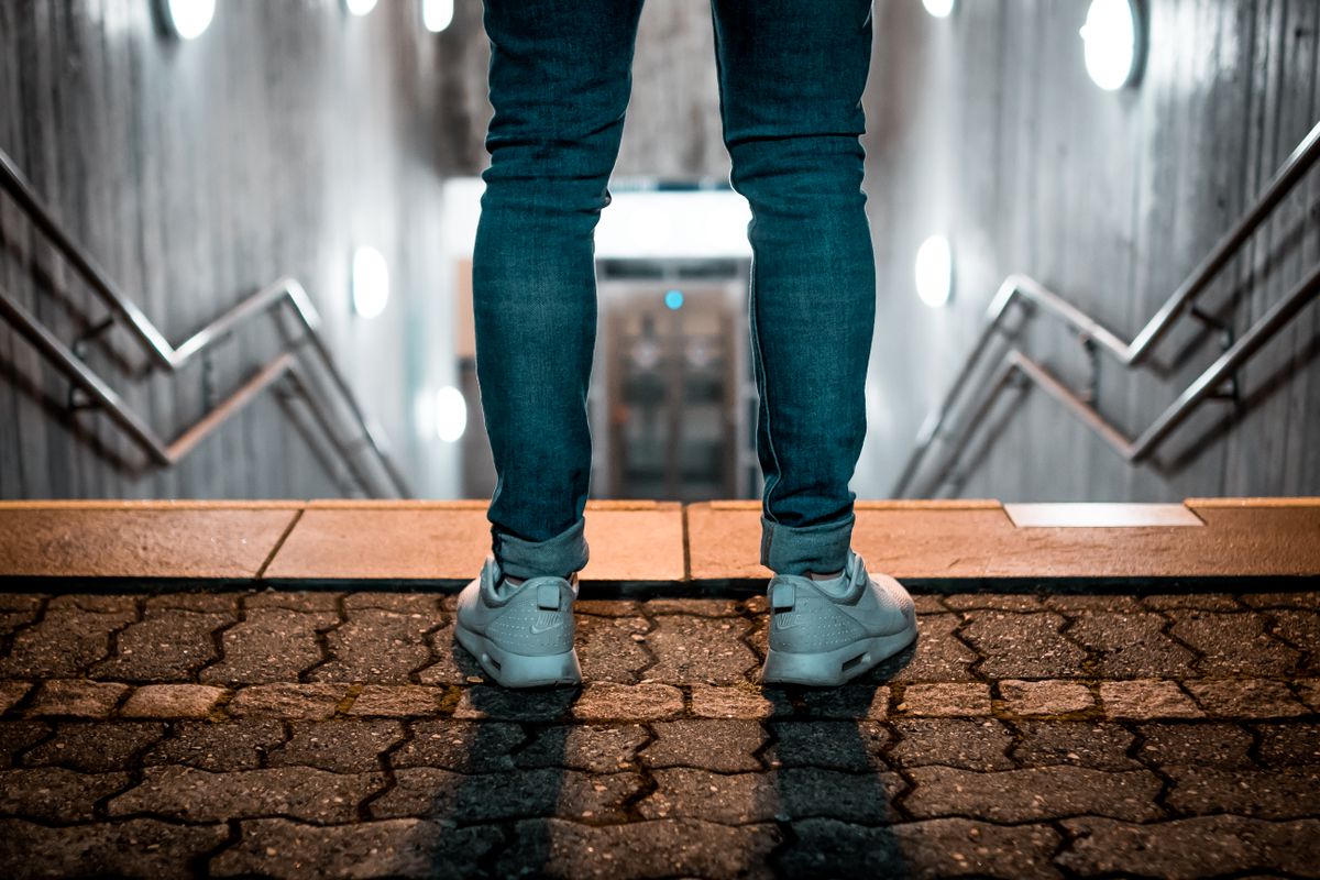 Person wearing sneakers stands at stairway entrance with modern lighting.