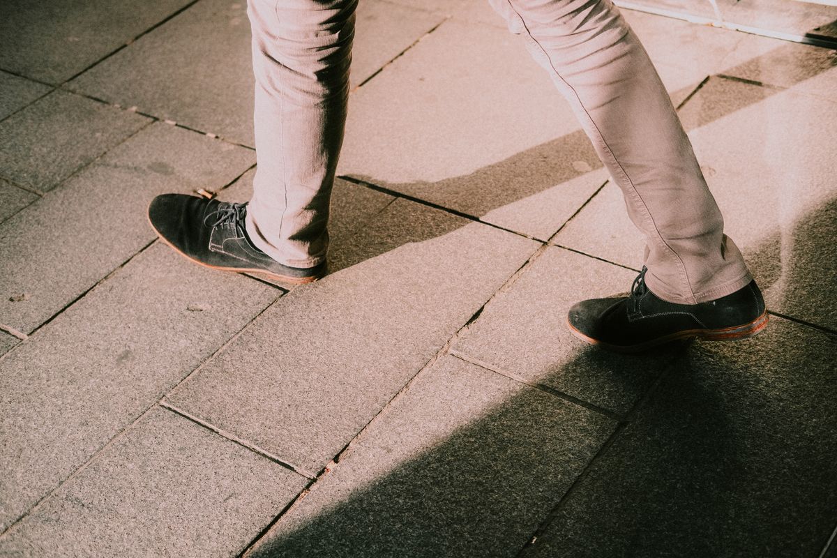 Close-up of legs in black shoes walking on stone pavement with shadows.
