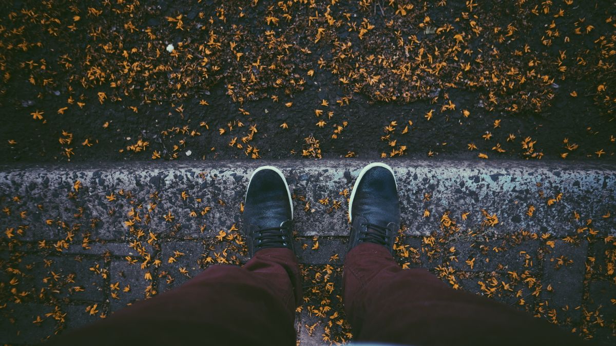 Top-down view of a person standing on a leaf-strewn pavement in autumn wearing stylish sneakers.
