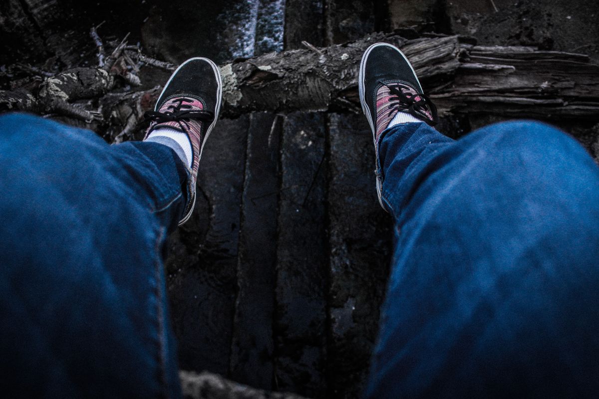 Person wearing sneakers and jeans sitting at cliff edge, overlooking a dam.