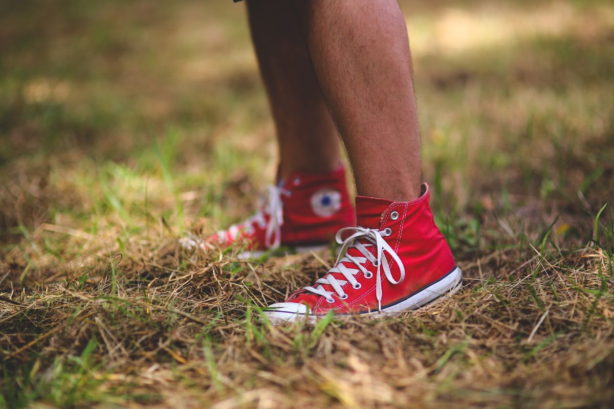 A person wearing red Converse sneakers stands on a grassy field, showcasing casual outdoor style.